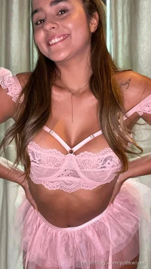 Woman in pink lace lingerie and tulle skirt, smiling, indoors.