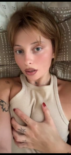 Woman with short brown hair and tattoos wearing tank top on bed