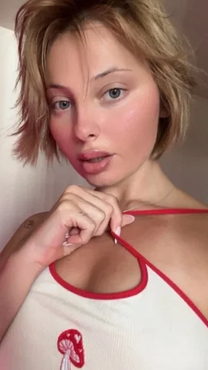 Woman with short blonde hair in white top with red trim, posing indoors.