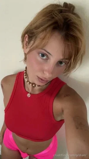 Woman with short blonde hair in red crop top and pink shorts, indoor selfie.