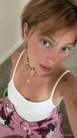 Woman with short brown hair in white tank top and pink floral skirt, indoor selfie.