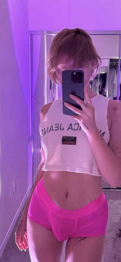 Short-haired blonde in white crop top and pink shorts mirror selfie.