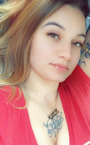 Blonde woman in red top with necklace and chest tattoos.