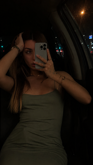 Woman in olive green dress taking mirror selfie in car at night.
