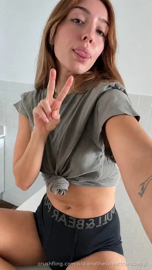 Woman in olive crop top and black shorts posing indoors, making peace sign.