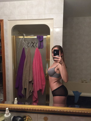 Woman in grey bra and black panties taking mirror selfie in bathroom.