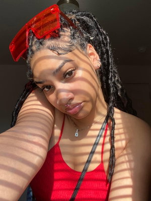 Woman with braided hair wearing red top and sunglasses indoors.