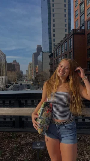 Woman with long blonde hair in striped top and denim shorts, standing outdoors on city balcony.
