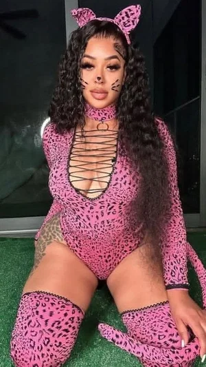 Woman in pink leopard print bodysuit with cat ears, posing on green surface indoors.