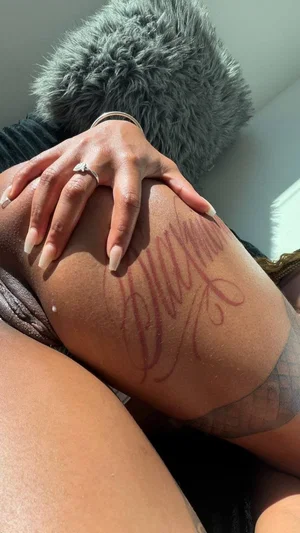 Woman with tattooed thigh and long nails, wearing dark clothing, indoors.