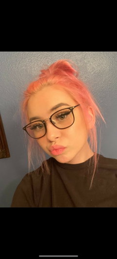 Woman with pink hair and glasses wearing a black top indoors.