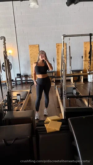Woman in black crop top and leggings takes mirror selfie in gym.