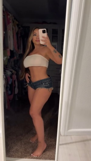 Curvy Asian woman in bandeau top and denim shorts, closet mirror selfie.