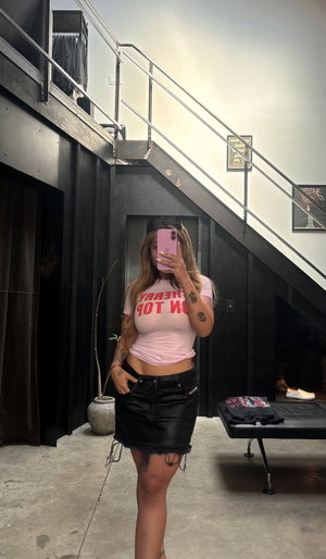 Tattooed woman in pink crop top and black mini skirt indoors.