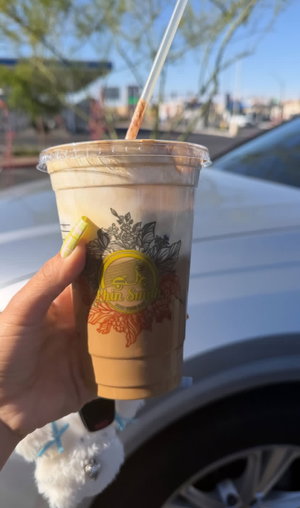 Hand with painted nails holds iced coffee cup by car.