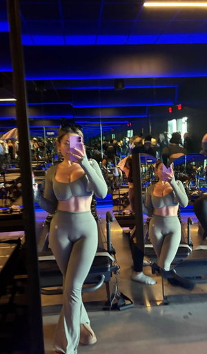 Curvy woman in gray crop top and leggings in gym mirror selfie.