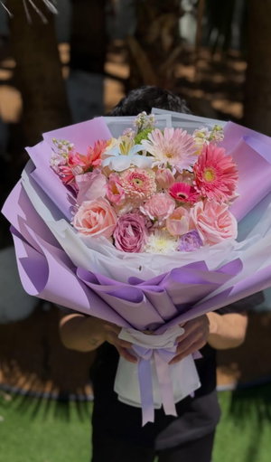 Person holding a large bouquet of pink and purple flowers outdoors, face obscured.