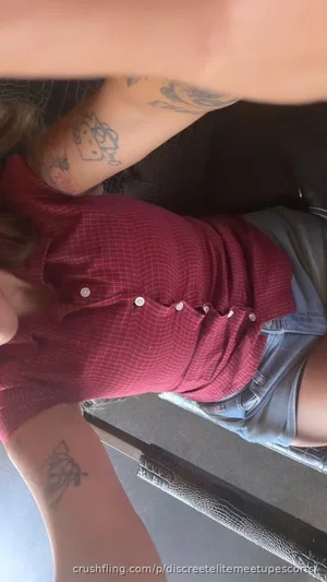 Person with tattoos wearing red shirt and denim shorts, lying on surface.