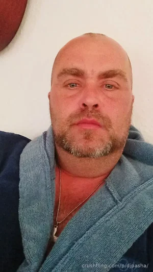 Bald man with beard wearing blue robe, indoors, looking at camera.