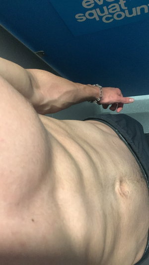 Muscular man in black shorts taking mirror selfie indoors.
