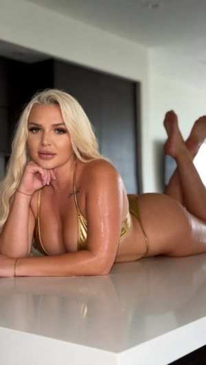 Blonde woman in gold bikini lying on white counter indoors.