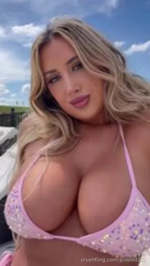 Woman with blonde hair in pink sequined bikini top, outdoors under blue sky.