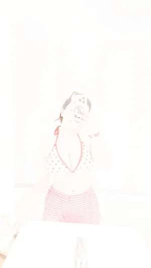 Woman in polka dot top and striped shorts takes mirror selfie in bright room.