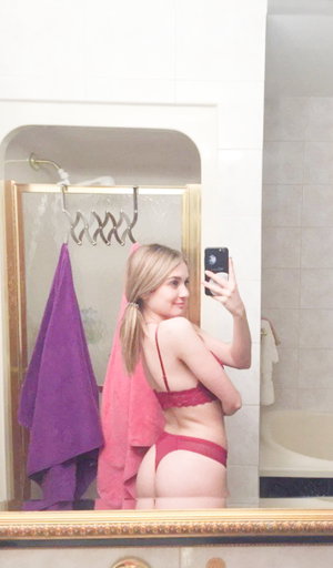 Blonde woman in red lingerie takes bathroom mirror selfie.