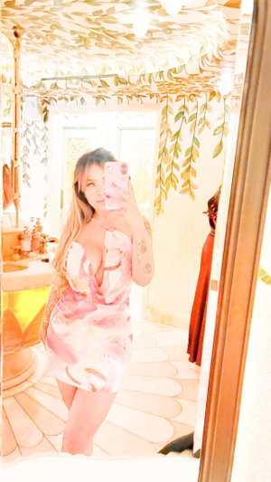 Woman in floral dress taking mirror selfie in leaf-patterned bathroom.