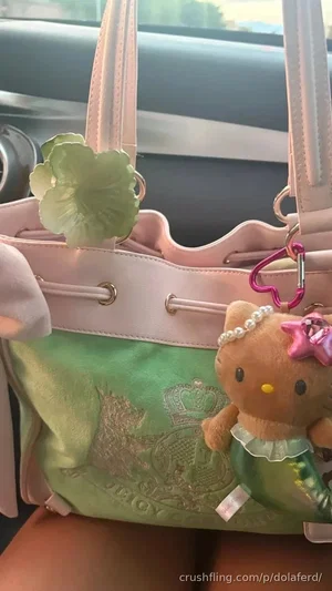 Pink and green handbag with Hello Kitty plush charm, held on lap in car.