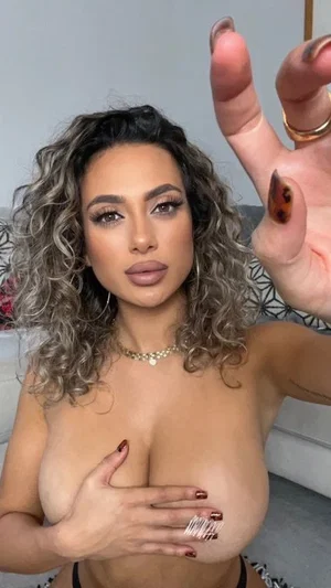 Woman with curly hair covering breasts, wearing black bottoms, indoors.
