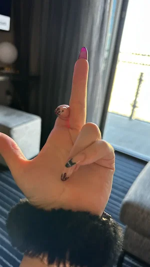 Hand with decorated nails and black fuzzy sleeve, indoors near window.