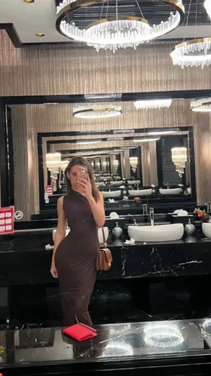 Woman in a brown dress taking mirror selfie in a luxury bathroom.