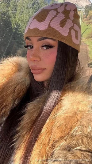 Woman with long dark hair wearing a camouflage beanie and fur coat outdoors.