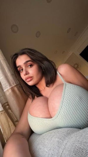 Woman with dark hair in light green top posing indoors on couch.