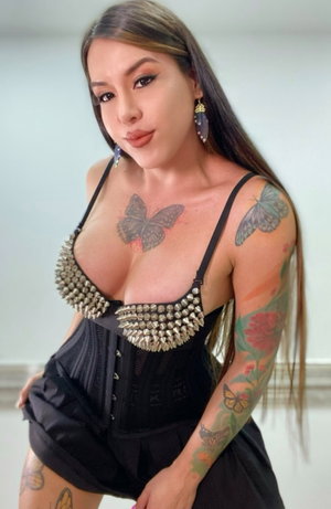Curvy woman in black studded corset and skirt with tattoos.