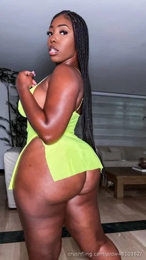 Woman with long braids in bright green dress posing indoors, showing back and buttocks.