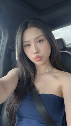 Woman with long dark hair in blue strapless top sitting in car, wearing seatbelt.