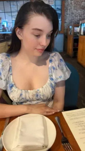 Woman in floral dress sitting at restaurant table, looking down at menu.