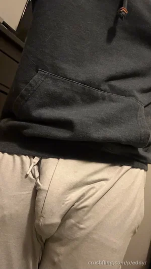 Person wearing dark hoodie and light pants, standing indoors.