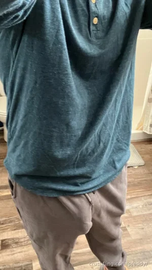 Person in teal henley shirt and gray pants standing indoors on wood floor.