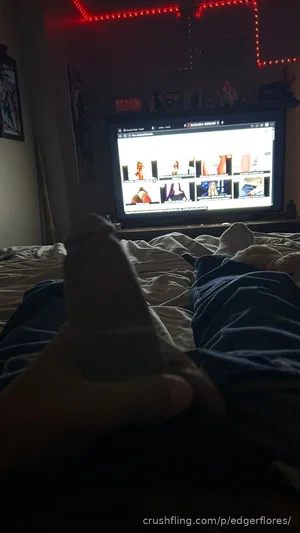 Person in socks lying on bed, feet in foreground, TV screen showing thumbnails in background.