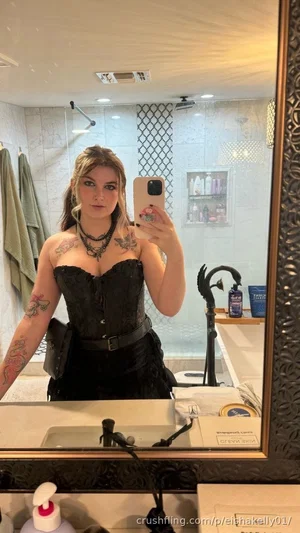 Woman in black corset and skirt takes mirror selfie in bathroom with tattoos visible.