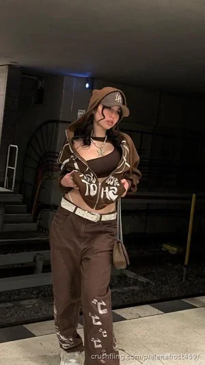 Woman in brown hoodie and matching pants, wearing crop top and cap, standing indoors.