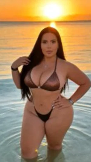 Woman in black bikini standing in shallow ocean water at sunset.
