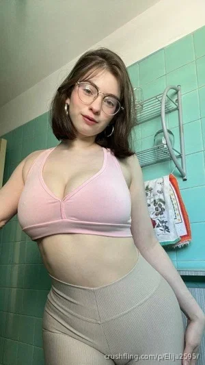 Woman in pink sports bra and beige leggings posing in a bathroom with teal tiles.