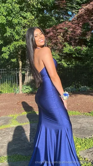 Woman in a blue strapless gown posing outdoors in a garden with trees and stone path.