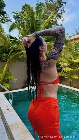 Woman with tattoos in red bikini by pool, dark hair, outdoor setting.