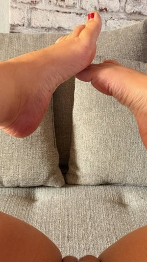 Woman's feet with red toenails on a gray couch.