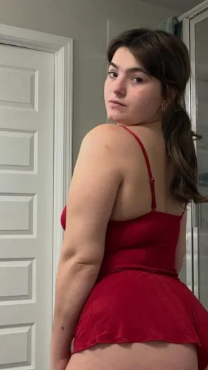 Woman in red dress posing indoors near door.